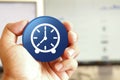 Clock icon blue round button holding by hand infront of workspace background Royalty Free Stock Photo