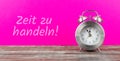 Clock with pink background with german text zeit zu handeln, in english time to act