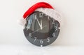 A clock in a Santa Claus hat on a white background shows five minutes to twelve Royalty Free Stock Photo