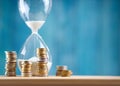 Clock with stacked coins and hourglass on blue background Royalty Free Stock Photo