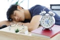 Clock on Table in front of Tired Asian man napping at a office after a hard workday.