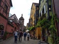 Clock tower and traditional Houses with colorful facades and sloping roofs in Riquewihr, France.