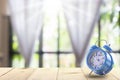 Clock on Wood table top on blur of window with curtain and garden flower background in morning Royalty Free Stock Photo