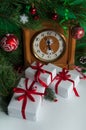 Clock in a wooden case, pine branches, gift boxes and red balls, streamers and white snowflakes on a white background.