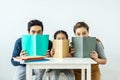 Asian young mother and father with little daughter sit at desk and holding book with funny facial expression