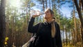 Cloesup portrait of beautiful hiking woman drinking water while travelling in pine forest