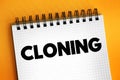 Cloning is the process of producing individual organisms with identical genomes, text concept on notepad