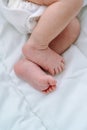 Close bare feet of newborn unrecognizable child in white clothes on light blanket. Skin care, baby care