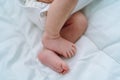 Close bare feet of newborn unrecognizable child in white clothes on light blanket. Skin care, baby care