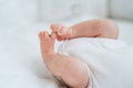 Close bare feet of newborn unrecognizable child in white clothes on light blanket. Skin care, baby care