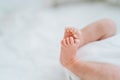 Close bare feet of newborn unrecognizable child in white clothes on light blanket. Skin care, baby care