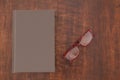 Close book with empty cover and a pair of glasses on a wooden table