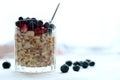 Close glass of granola oatmeal with chia, cranberry and american blueberries on table