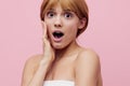 a close horizontal beauty photo on a pink background of a surprised woman with her hair pinned up from behind, looking