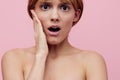 a close horizontal beauty photo on a pink background of a surprised woman with her hair pinned up from behind, looking