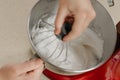 A close photo of the hand of a woman who is mixing meringue in a bowl