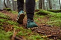 Close photo of a tourist`s feet in boots walking on wet ground with moss in the woods during a hike in the woods Royalty Free Stock Photo