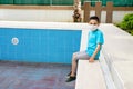 A boy with medical mask sits by an empty pool. Concept summer 2020. No tourism