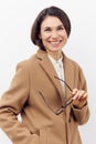 close portrait of a beautiful, happy woman in a brown coat with glasses in her hand, smiling cutely at the camera while Royalty Free Stock Photo