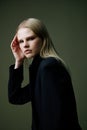 A close portrait of a blonde looking over her shoulder in a black jacket posing in a studio on a green background. The Royalty Free Stock Photo