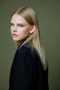 A close portrait of a blonde looking over her shoulder in a black jacket posing in a studio on a green background. The Royalty Free Stock Photo