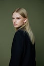 A close portrait of a blonde looking over her shoulder in a black jacket posing in a studio on a green background. The Royalty Free Stock Photo