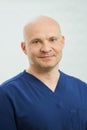 A close portrait of a caucasian bald adult dentist in the navy blue uniform