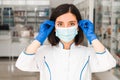 Close portrait female pharmacist in pharmacy putting on face a protective mask getting to work to help people Royalty Free Stock Photo