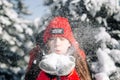 Close portrait of a girl teenager wearing red jacket and hat and blowing the snow out of her hands at the winter park. Young woman Royalty Free Stock Photo