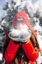 Close portrait of a girl teenager wearing red jacket and hat and blowing the snow out of her hands at the winter park. Young woman Royalty Free Stock Photo