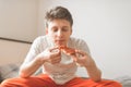 Close portrait of a guy sitting in bed with a piece of pizza in his hands, eating with his eyes closed. Fast Food, Pizza Concept.