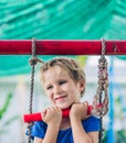 Close portrait Happy smile freckle blue eyed cute blond little boy sitting on a rope ladder, playing outside on