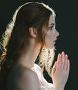 A close portrait of a praying young red-haired woman in a vintage ash dress with open shoulders on a black background in backlight Royalty Free Stock Photo