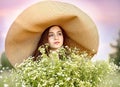Close portrait young beautiful girl in a big wicker hat with a huge bouquet of chamomile in a daisy field at sunset. Flowers and Royalty Free Stock Photo