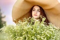 Close portrait young beautiful girl in a big wicker hat with a huge bouquet of chamomile in a daisy field at sunset. Flowers and Royalty Free Stock Photo