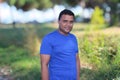 Close portrait of young man in blue t shirt standing outside in park with trees in background Royalty Free Stock Photo