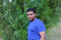 Close portrait of young man in blue t shirt standing outside in park with trees in background Royalty Free Stock Photo