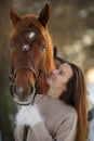 Close portrait of young smiling woman and brown horse at winter sunset. Woman with long hear in sweater near big horse Royalty Free Stock Photo