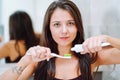 Close is portrait of young woman holding toothpaste and a toothbrush. Feemale look into camera and smile with a snow