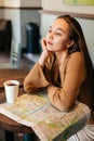 Close portrait of young woman with paper map sitting at table with cup of coffee at old town cafe Royalty Free Stock Photo