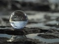 Close shot of a glass sphere reflecting the water in the middle of the rocks under a blue sky Royalty Free Stock Photo