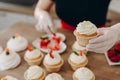 Close shot of many sweet cupcakes on the foreground while a baker decorating the last one.