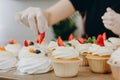 Close shot of many sweet cupcakes on the foreground while a baker decorating the last one.