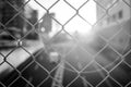 Close shot of the sun shining through a metal fence with blurred background in black and white Royalty Free Stock Photo