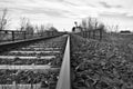 Close shot of train tracks in rocks near leafless trees under a cloudy sky in black and white Royalty Free Stock Photo