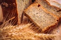 Close slice of fresh bread with poppy seeds and wheat ears on wooden background