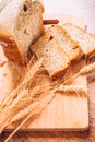 Close slice of fresh bread with poppy seeds and wheat ears on wooden background