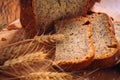 Close slice of fresh bread with poppy seeds and wheat ears on wooden background