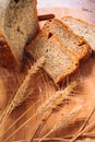 Close slice of fresh bread with poppy seeds and wheat ears on wooden background