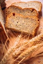 Close slice of fresh bread with poppy seeds and wheat ears on wooden background